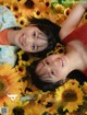 A couple of young women laying on top of a bed of sunflowers.