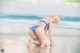 A woman in a bikini kneeling on the beach.